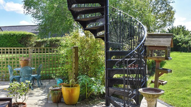 A spiral staircase in a garden setting with potted plants and outdoor furniture. - Church View Apartment (Parkham, near Bideford)