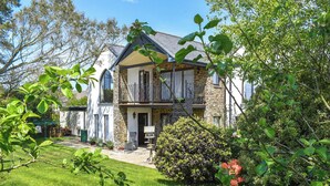 A two-story house with a stone facade, a balcony with metal railings, and a well-maintained garden. - Church View Apartment (Parkham, near Bideford)