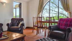 A room with a large window, a wooden dining table, and two leather armchairs. - Church View Apartment (Parkham, near Bideford)