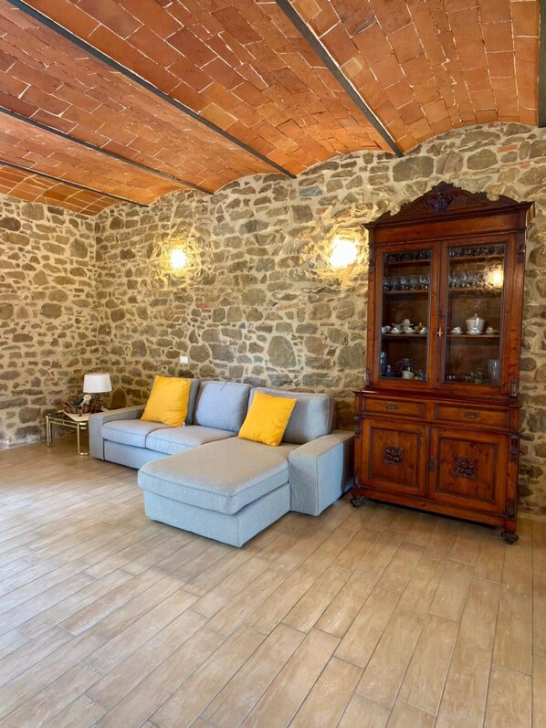 Une pièce avec un mur en pierre, un meuble en bois et un canapé bleu clair agrémenté de coussins jaunes.