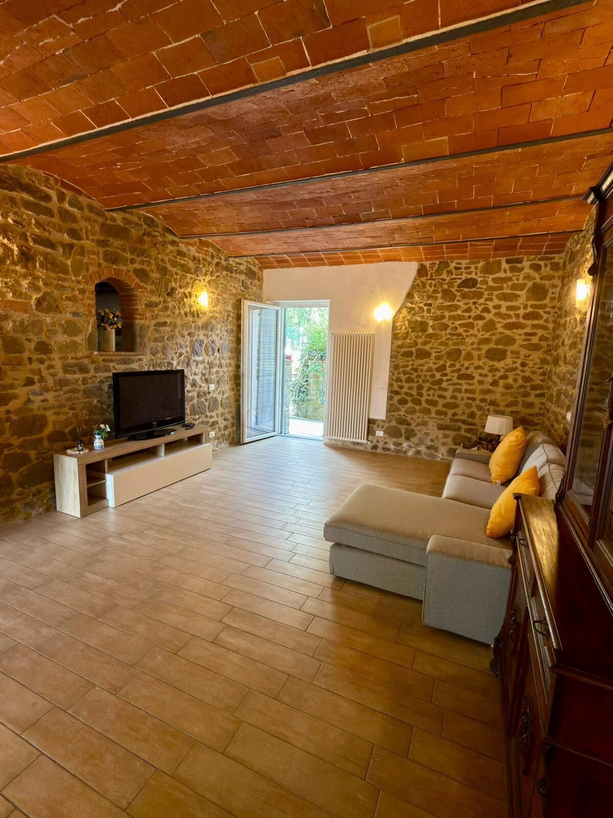 A spacious living room with a stone wall, a television, a sofa, and a wooden ceiling.
