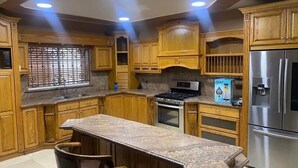 Una cocina con armarios de madera, un refrigerador de acero inoxidable, una estufa a gas y una encimera de granito.