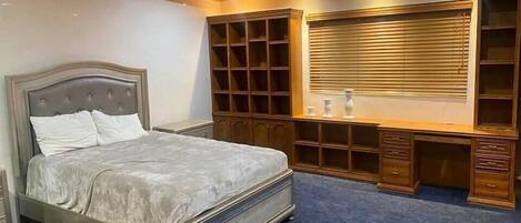 Un dormitorio con una cama grande, estanterías empotradas, un escritorio y una ventana con persianas.
