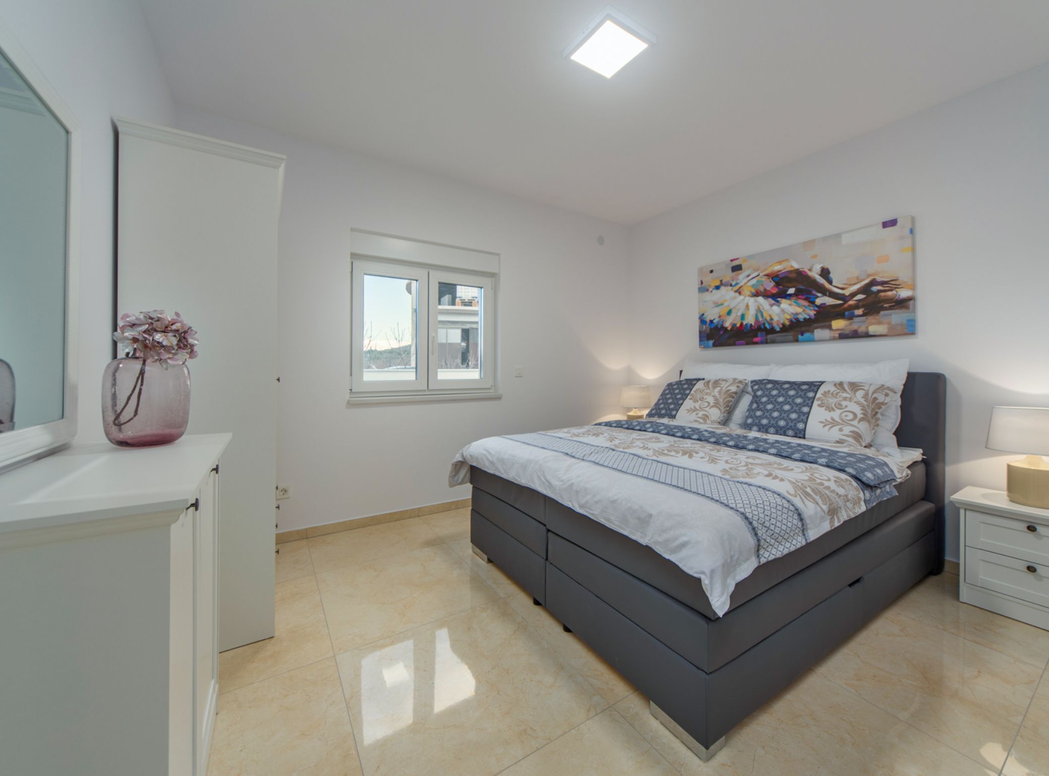 Un dormitorio con cama, mesitas de noche, una ventana y un cuadro en la pared.