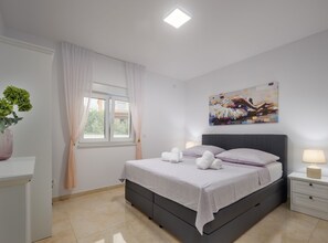 A modern bedroom with a bed, bedside tables, a window with curtains, a painting on the wall, and a potted plant. - Villa Shaula 2 (Bilice)