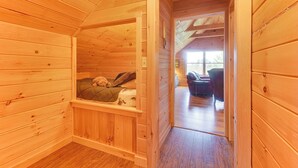 Una cabaña de madera con habitación en la buhardilla, que incluye una cama, una ventana y vistas al exterior.