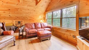 Un acogedor interior de cabaña con paredes de madera, un ventanal grande, un sofá de cuero y una televisión.