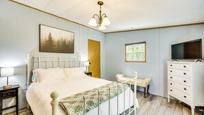 A bedroom with a bed, bedside table, lamp, dresser, TV, window, and a painting on the wall. - Hike, Fish & Ski: ‘Black Bear Cabin’ in Albany (Albany)