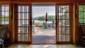 Una cabaña de madera con un balcón, mobiliario exterior y vistas a un lago y montañas.