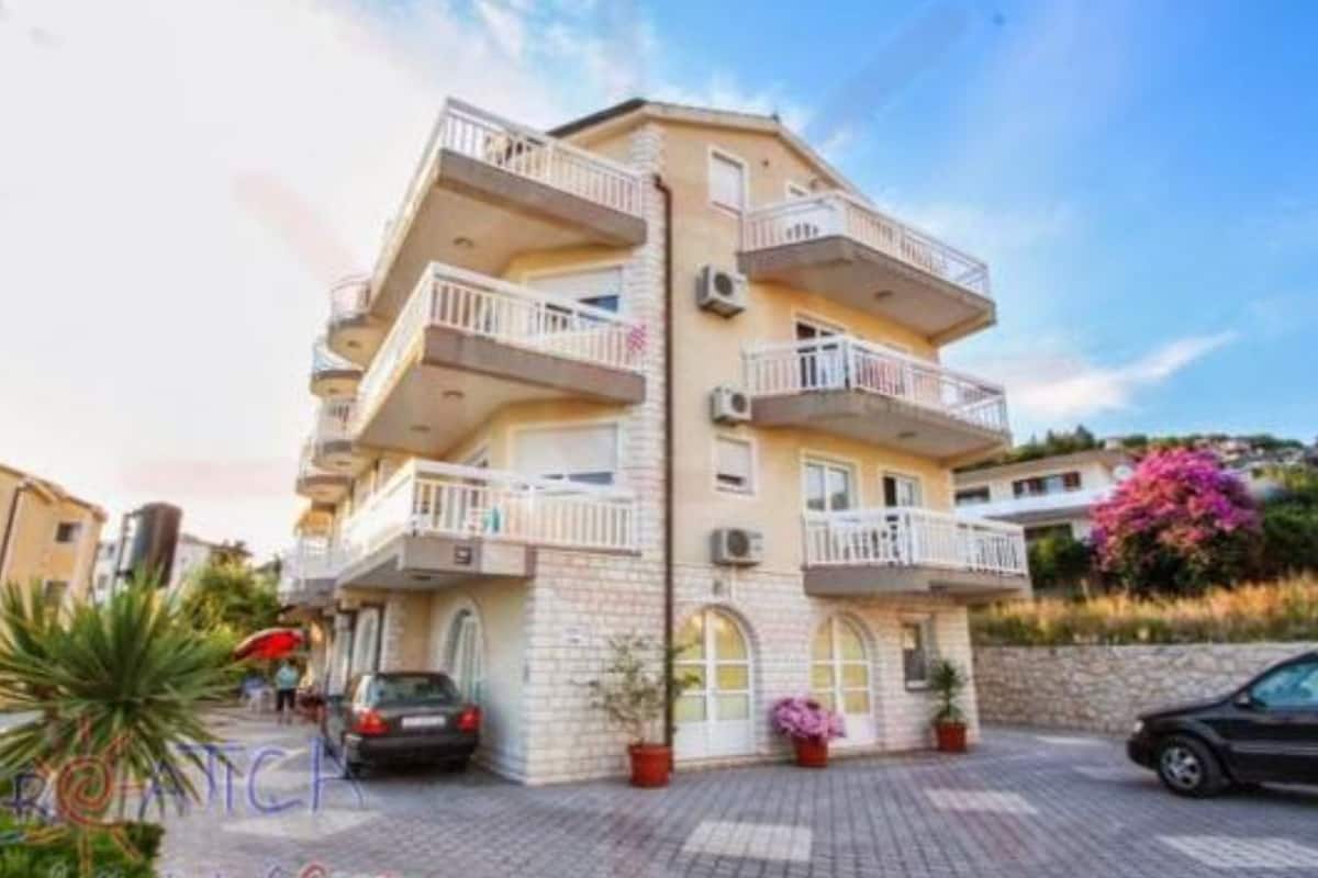 A multi-story building with balconies, a paved driveway, and potted plants.