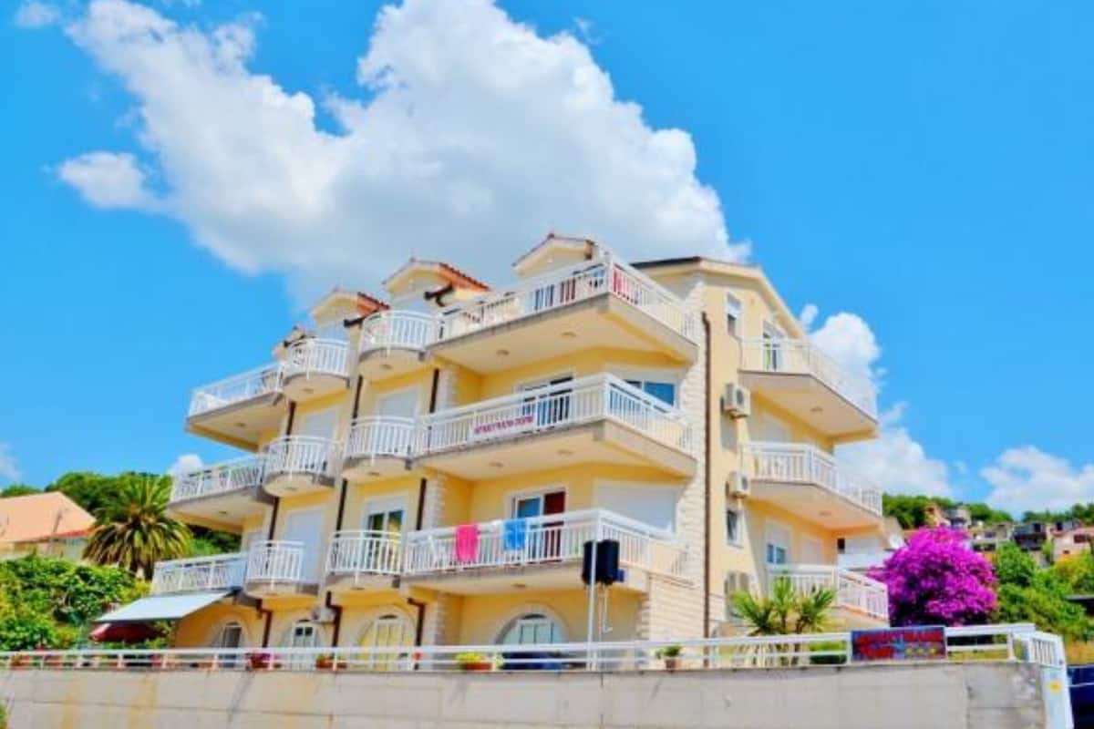 A multi-story hotel with balconies, a clear blue sky, and a palm tree in the background.