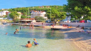 A beach with clear water, people swimming and playing, and buildings in the background. - Villa Tomi (Trogir)