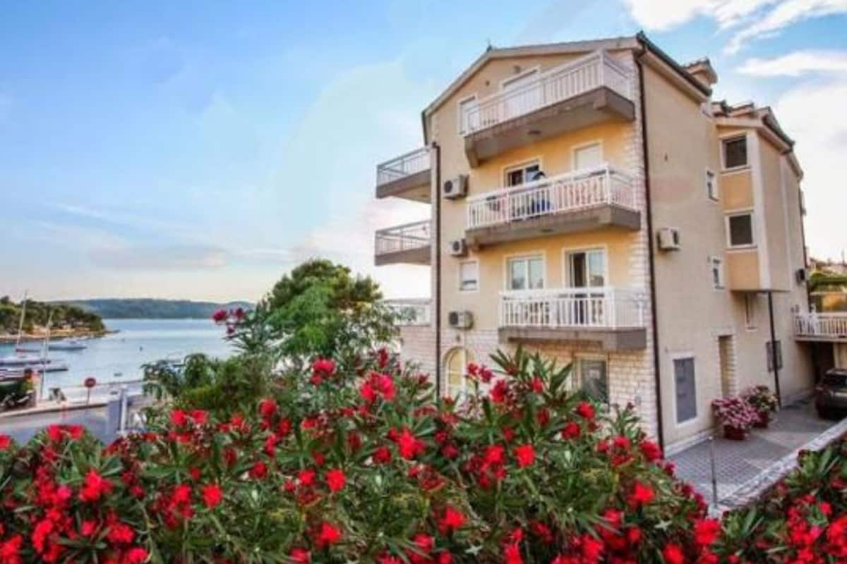 A multi-story building with balconies, a view of the sea, and red flowering plants in the foreground.
