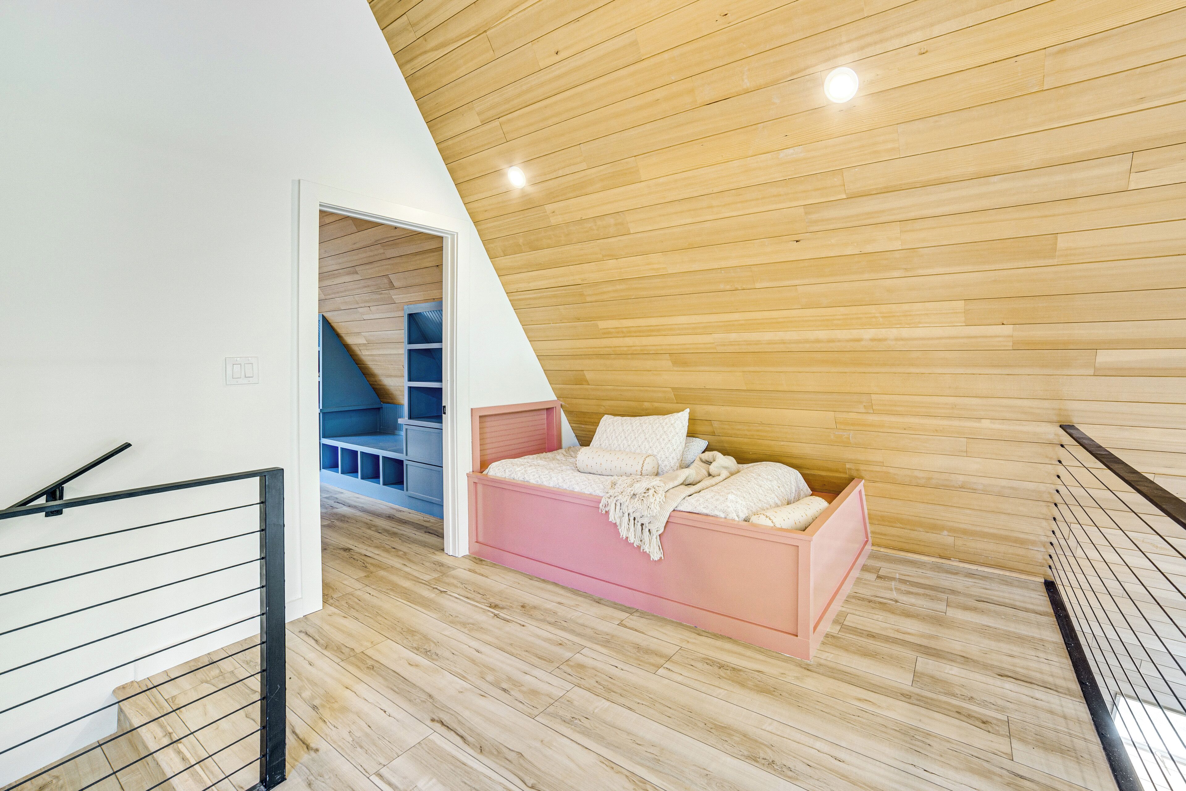 Een slaapkamer met een schuine kap, een roze bed en een houten vloer.