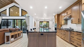 Een moderne keuken met houten kastjes, een centraal eiland en een eethoek met een glazen tafel en stoelen.