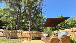 Un cortile con un patio in legno, mobili in vimini e un ombrellone grande.