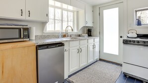Una cucina con mobili bianchi, lavastoviglie, forno a microonde, piano cottura e una finestra.