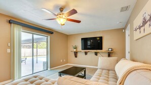 Ein Wohnzimmer mit Deckenventilator, einem flachbildfernseher an der Wand, einem Sofa und einem Couchtisch.