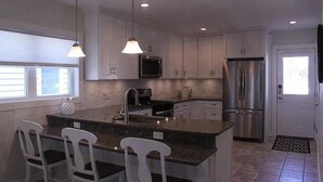 Una cocina moderna con armarios blancos, un refrigerador de acero inoxidable, un horno empotrado y una isla grande con taburetes de bar.