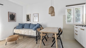 Une cuisine moderne avec une table à manger, des chaises et un canapé avec des coussins. Des tableaux encadrés ornent le mur, et un luminaire suspendu éclaire la pièce.