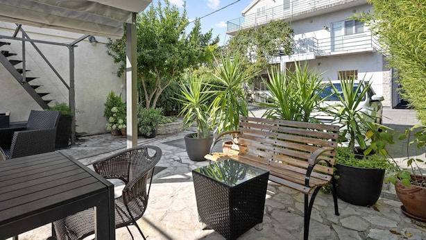 Un espace extérieur aménagé en terrasse, avec un banc en bois, des chaises en osier et une table à plateau en verre.