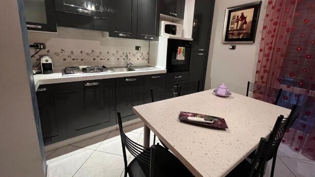 A compact kitchen with dark cabinets, a microwave, and a gas stove. There is a dining table with chairs and a small decorative item on it. - Charming 2-bedroom apartment with completed kitchen, nera Milano, Como and Swiss (Mozzate)