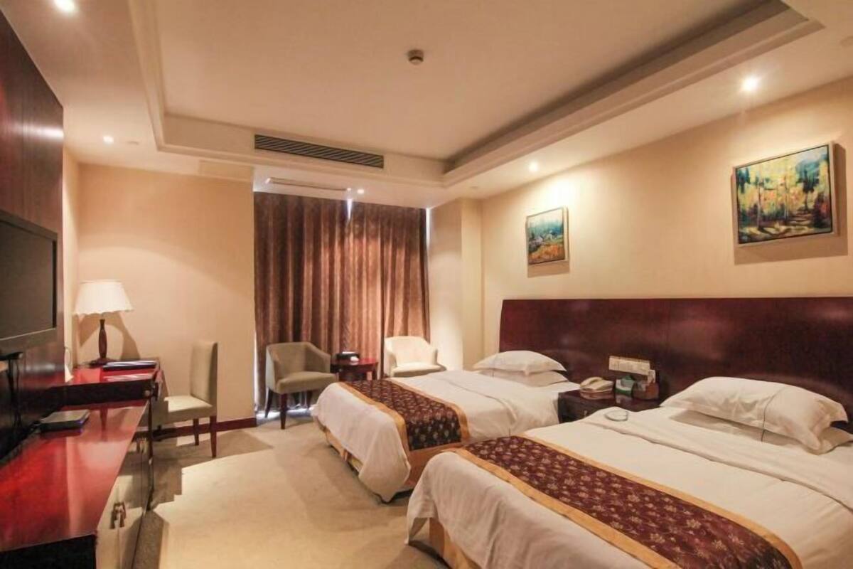Une chambre d’hôtel avec deux lits, un bureau, une chaise, une télévision et des œuvres d’art accrochées aux murs.