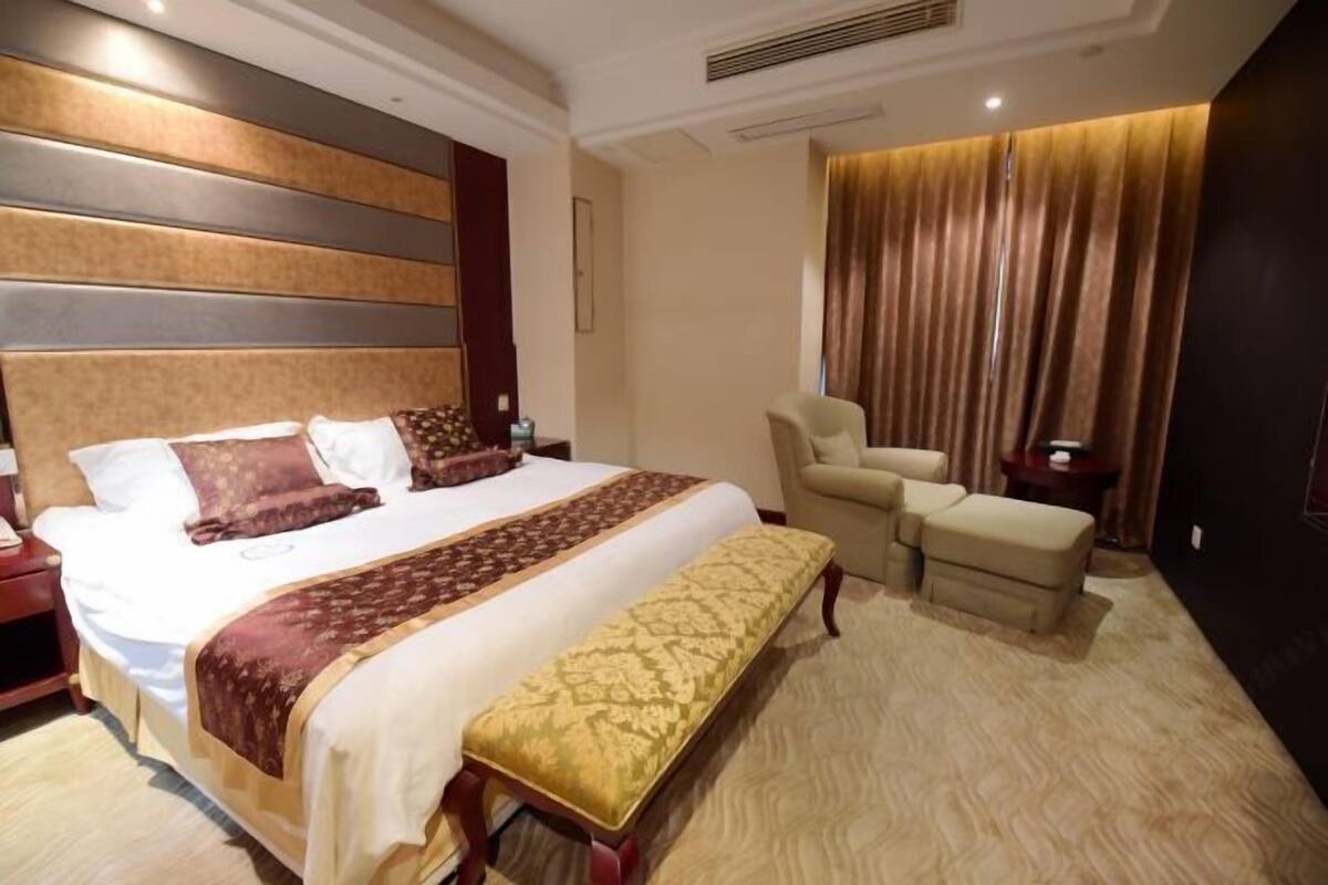 Une chambre d’hôtel avec un grand lit, un banc, une chaise et une petite table.