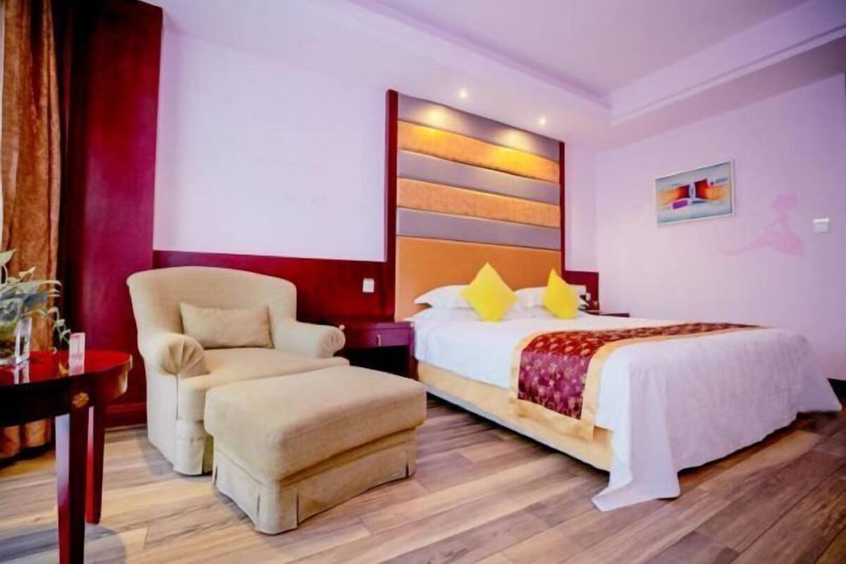 Une chambre d’hôtel comprenant un lit, une chaise, une table de chevet et un luminaire fixé au mur.