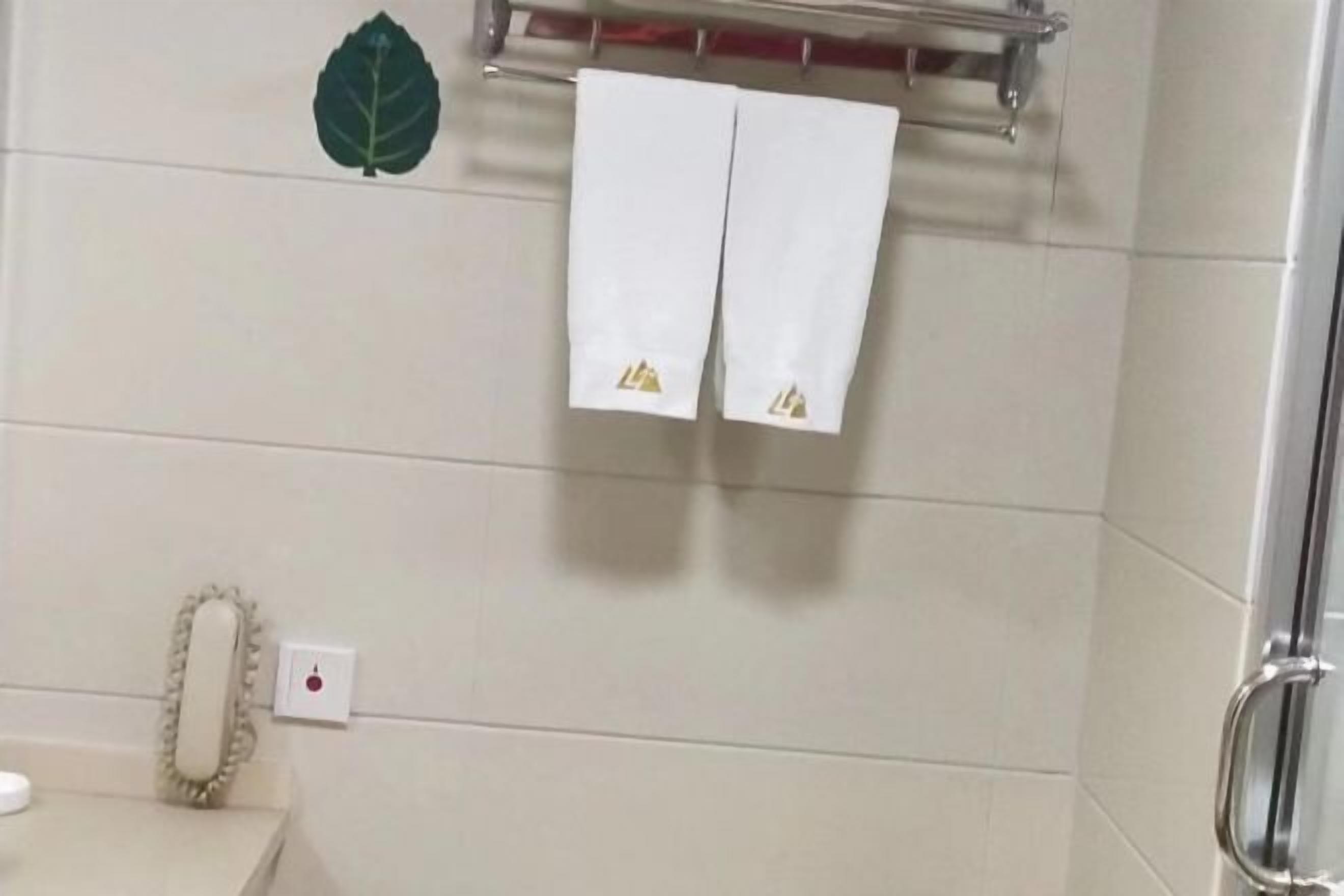 A bathroom with white tiles, a towel rack with two towels, a green leaf decoration, and a mirror with a decorative frame.