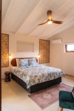 A bedroom with a bed, a ceiling fan, a nightstand, a chair, and artwork on the walls.