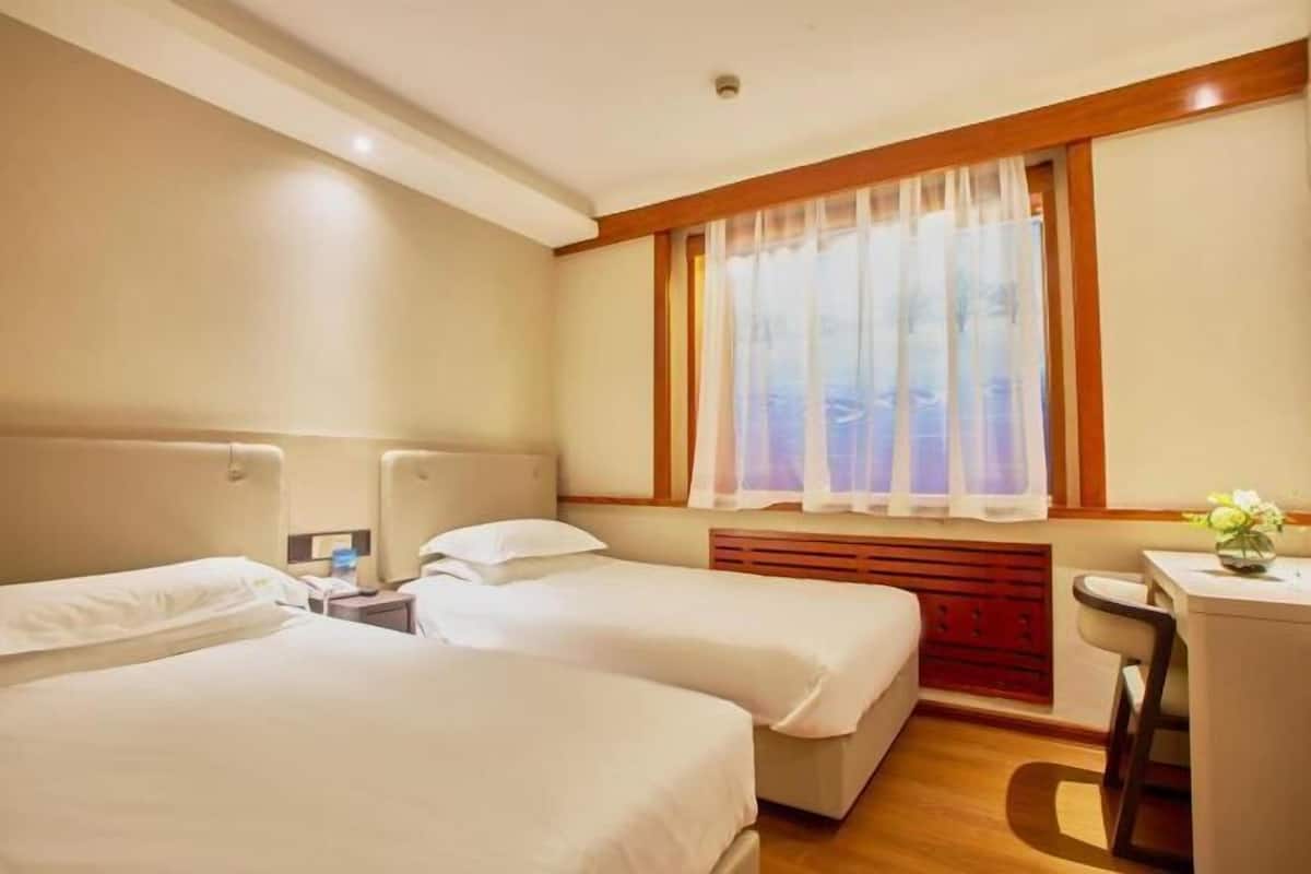 A hotel room with two beds, a desk, and a window with curtains.