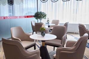 A hotel room with a seating area featuring round tables and chairs, a potted plant, and a view of the outside. - Harbin Gangcheng Hotel (Engineering University Subway Station) (Harbin)