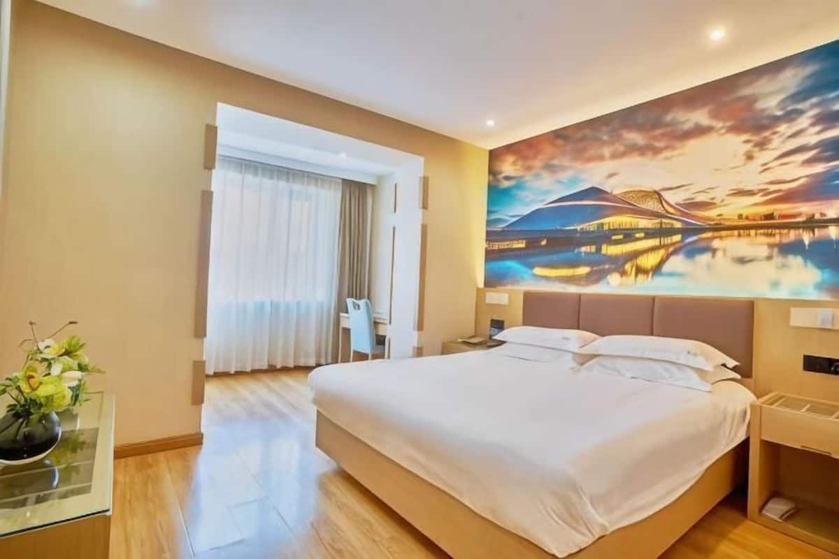 A hotel room with a large bed, a desk with a chair, a nightstand, and a wall mural.