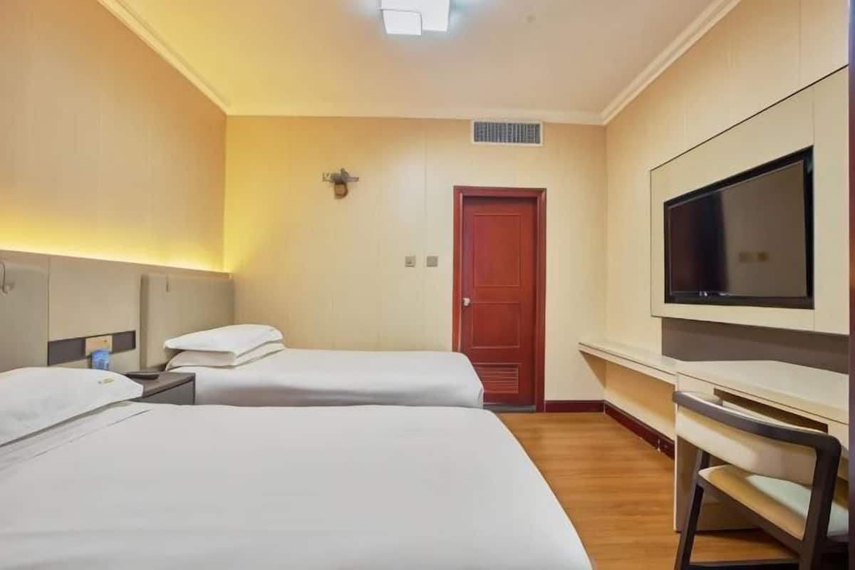 A hotel room with two beds, a desk, a chair, a TV, and a door.