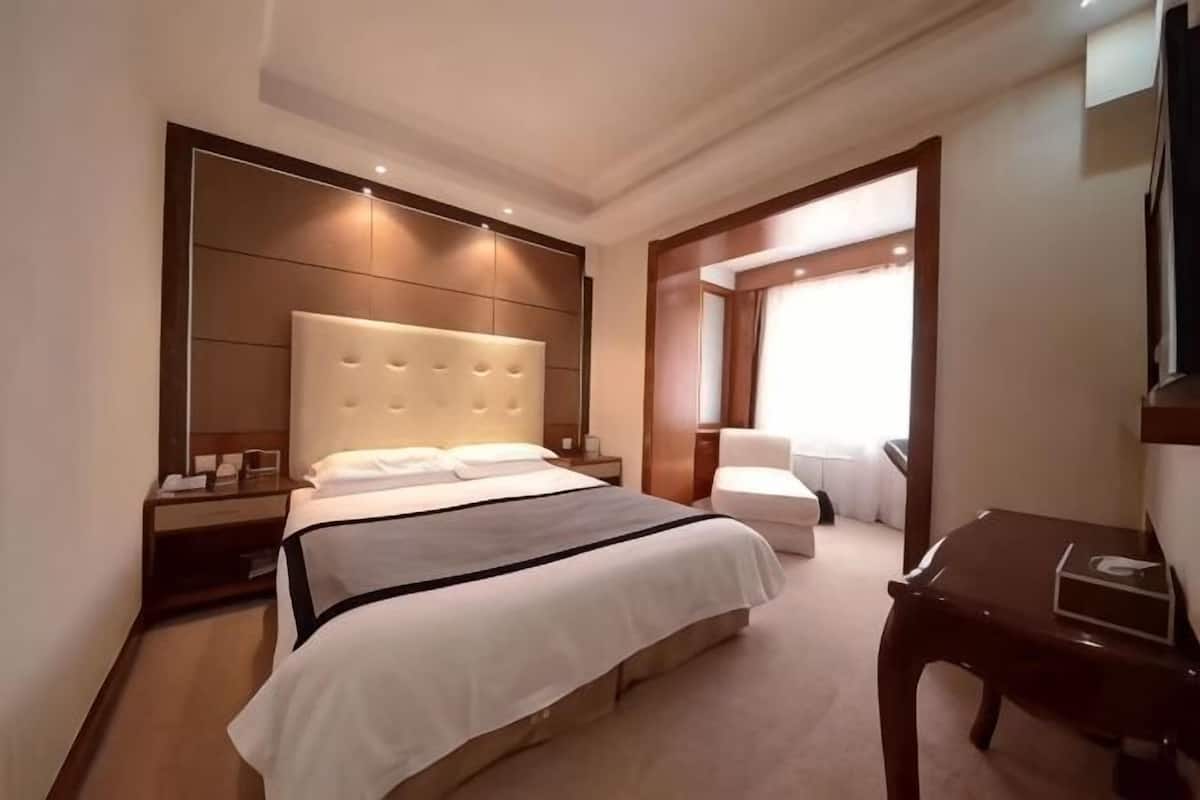 A modern hotel room with a large bed, a bedside table, a chair, and a desk.