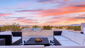 Eine Dachterrasse mit Gartenmöbeln, einem Pool und Blick auf den Sonnenuntergang.