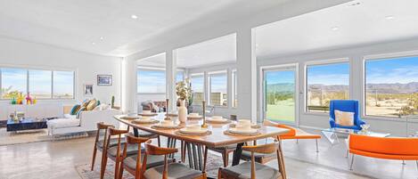 Un comedor espacioso con una gran mesa dispuesta para seis personas, rodeada de sillas. La habitación cuenta con ventanas amplias que ofrecen vistas al exterior.