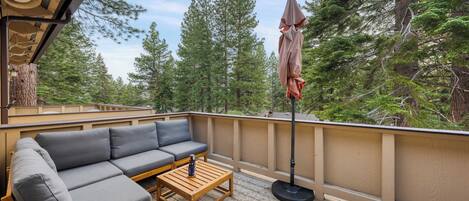 A covered outdoor deck with a gray sofa, wooden table, and umbrella.