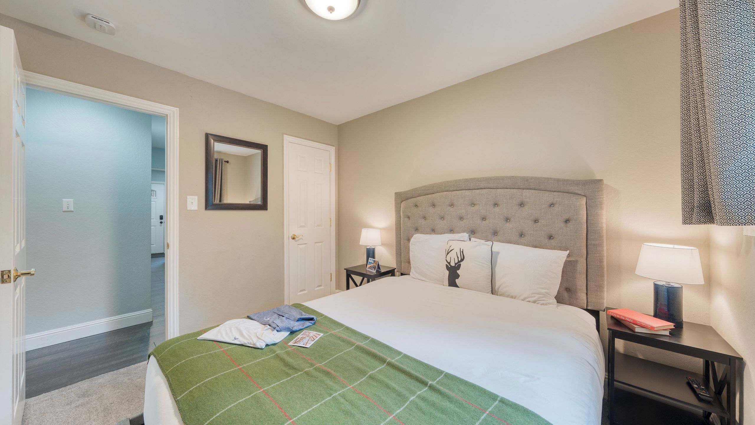 A hotel room with a bed, a nightstand, a lamp, a mirror, and a door.