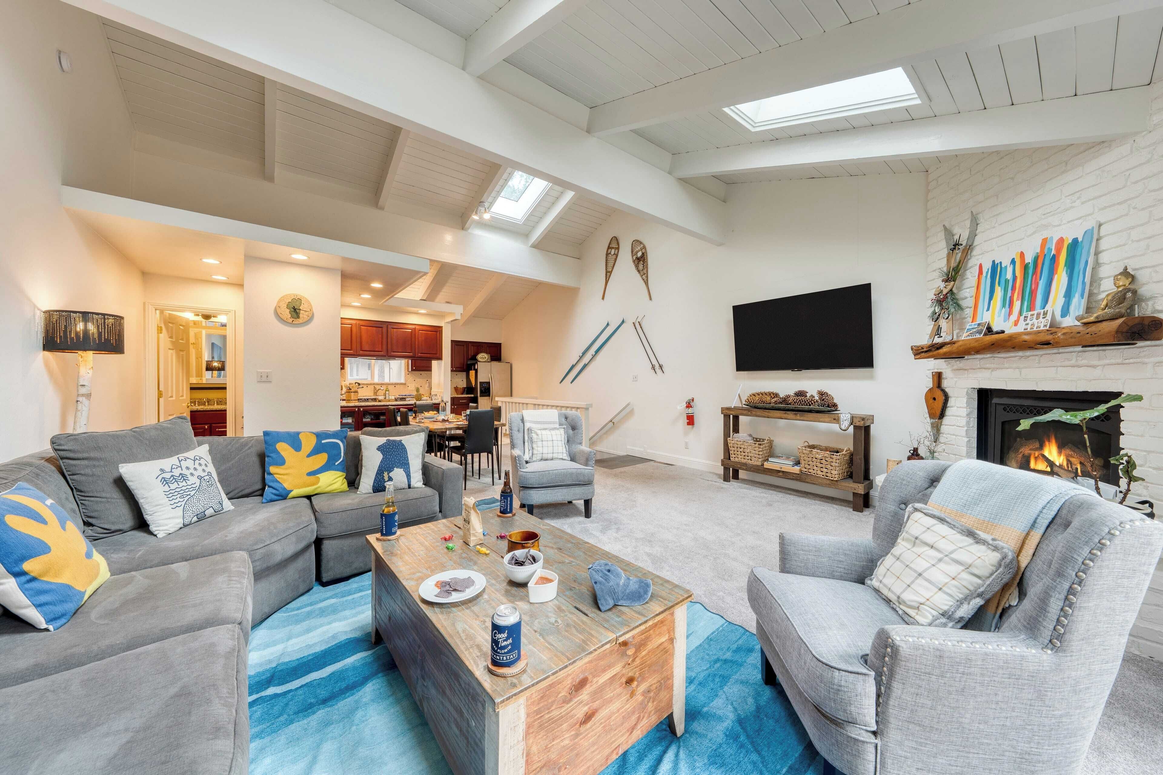 A spacious living room with a fireplace, a dining area, and a kitchen in the background.
