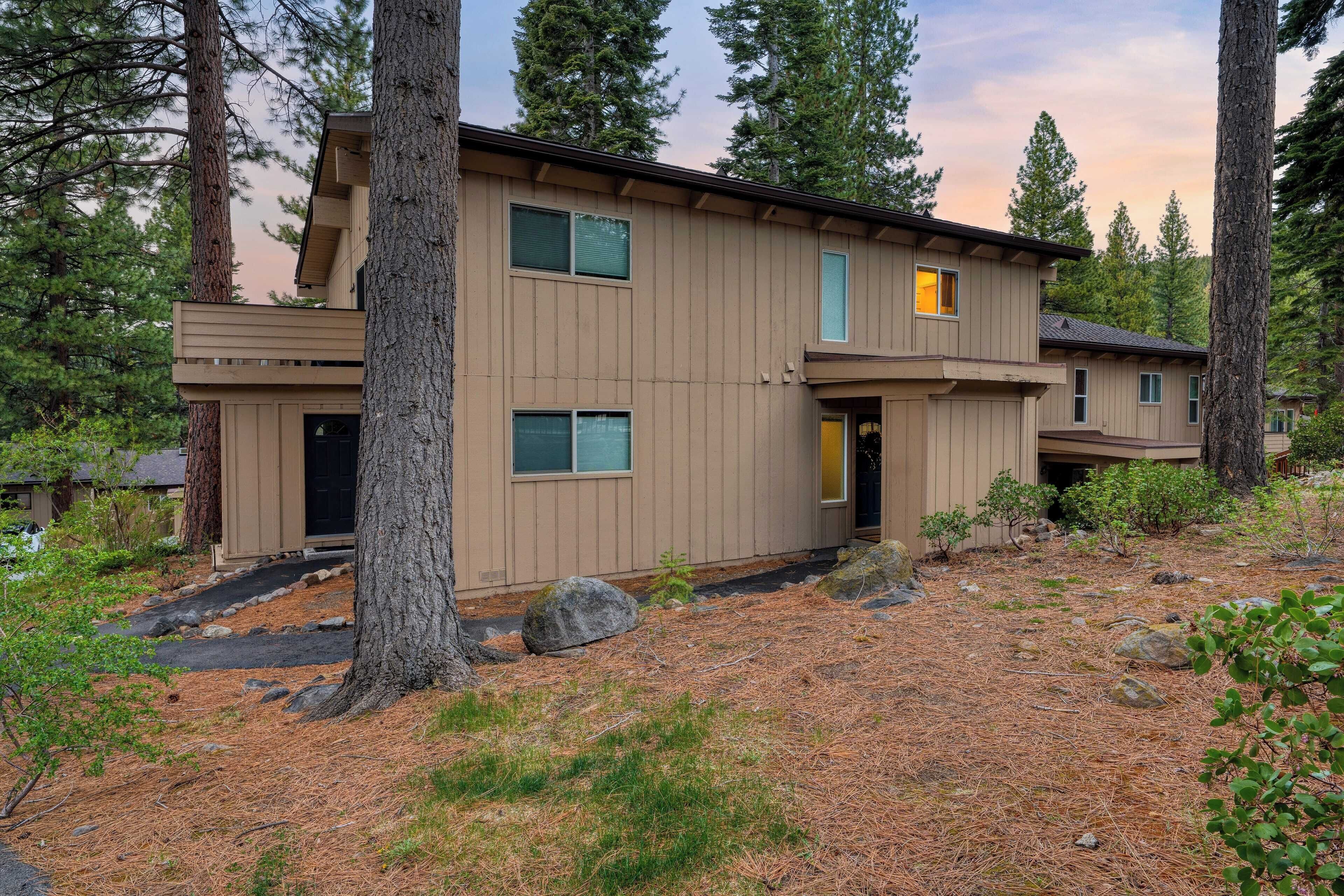 A two-story building with a flat roof, surrounded by tall trees and a pine needle-covered ground.