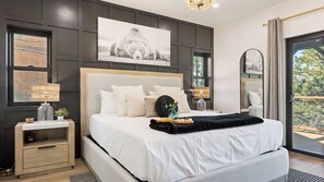 Ein modernes Schlafzimmer mit einem großen Bett, Nachttischen, einer Kopfteil und Blick auf Bäume durch ein Fenster.