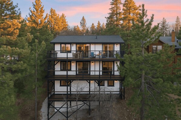 A two-story house with a balcony on the upper floor, surrounded by trees.