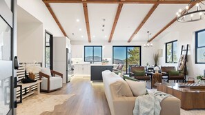 A spacious living area with a large sofa, a dining table, and a kitchen in the background. - Modern Lodge Near Lake, Village, & Snow Summit Game Room, Decks, Firepit, Views (Big Bear City)