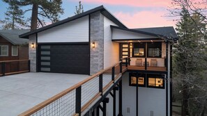 Ein modernes, zweistöckiges Haus mit Garage, einem Balkon mit Geländer und einem großen Fenster mit Blick auf die Terrasse.