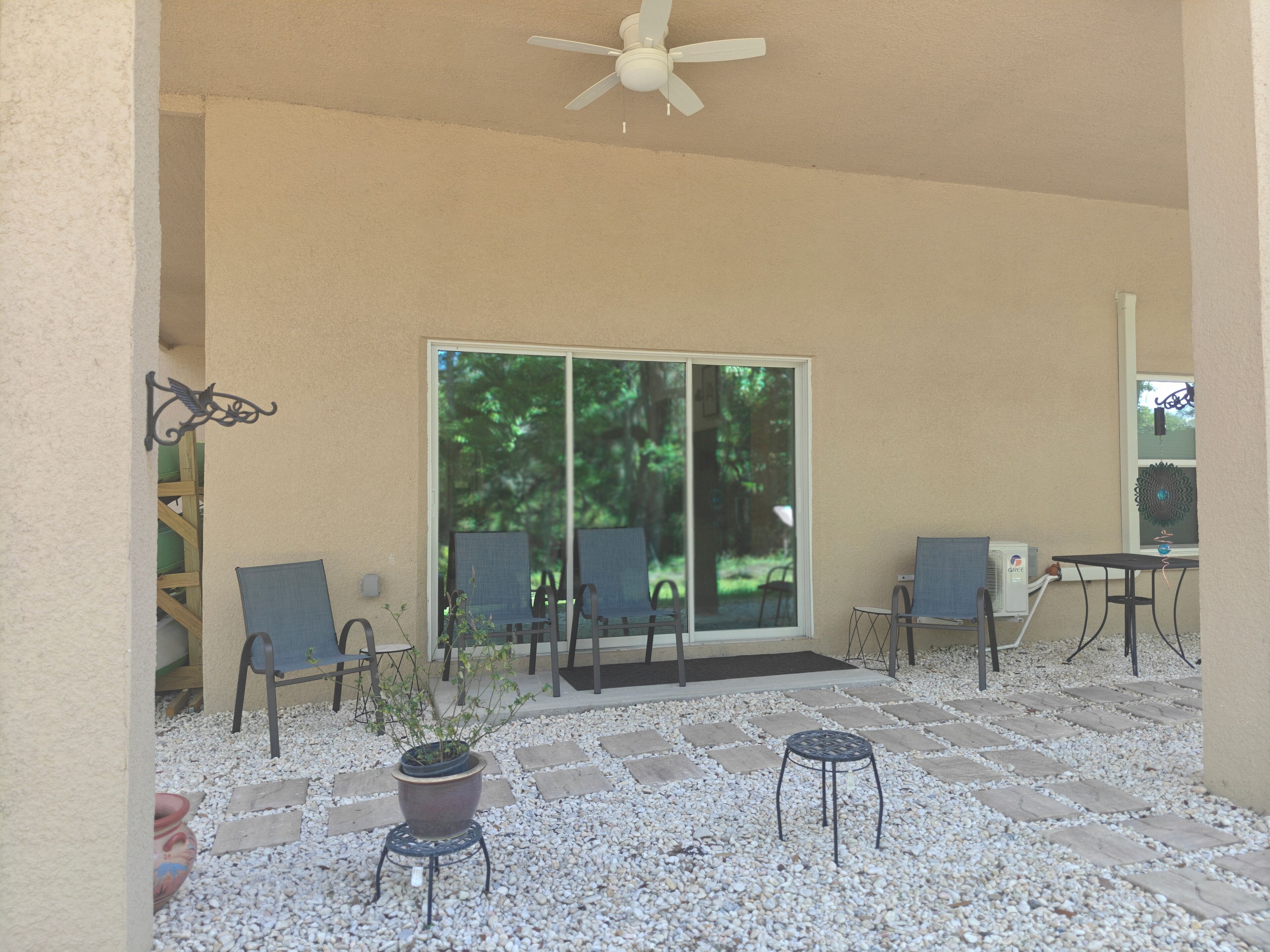 A covered patio with a ceiling fan, two chairs, a small table, and a potted plant.