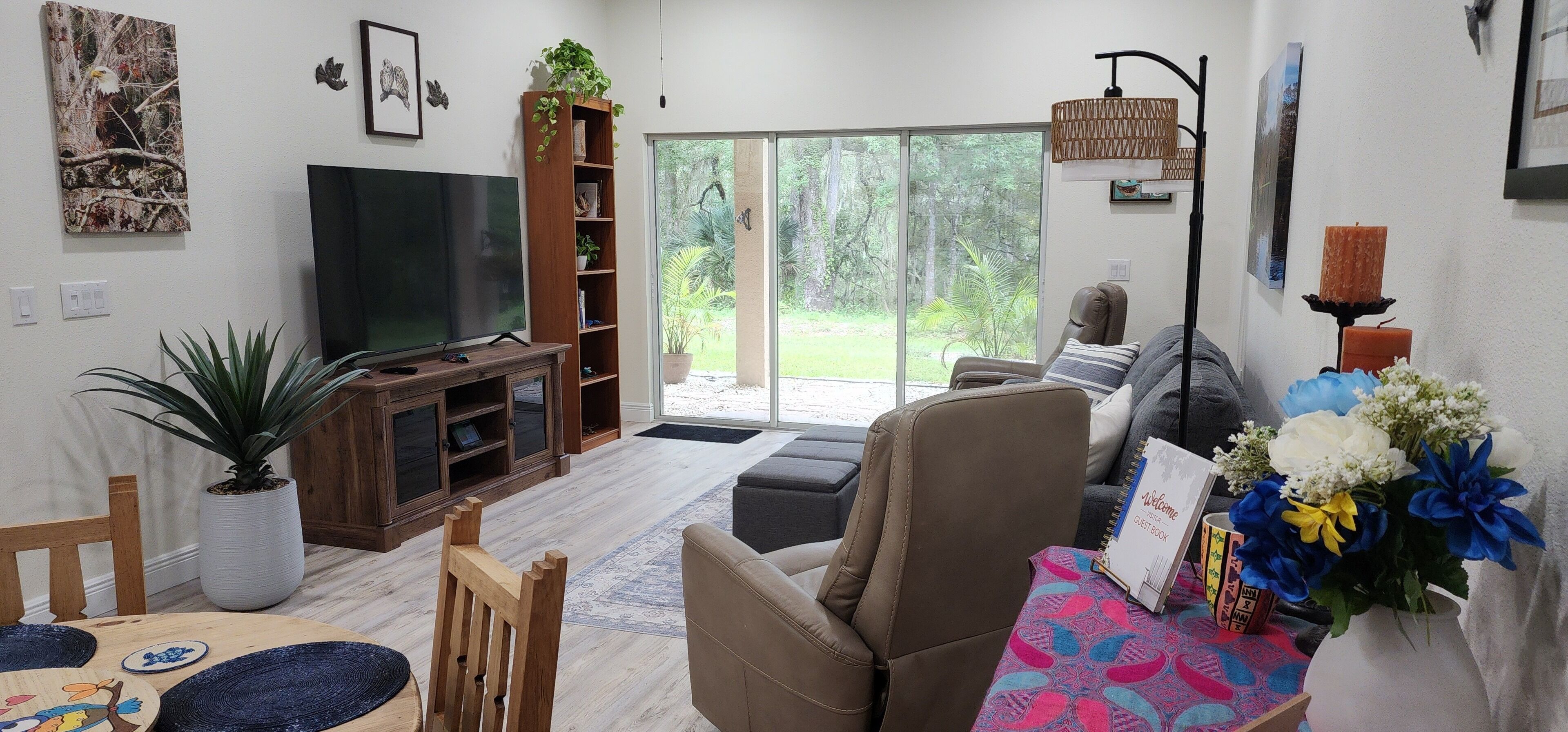 A living room with a TV, a bookshelf, a sofa, a coffee table, and a view of the outdoors.