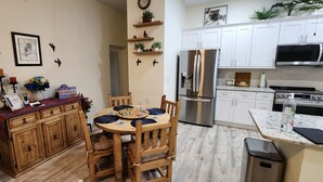 A compact kitchen with white cabinets, a stainless steel refrigerator, a microwave, and a stove. There is a dining table with chairs and a small trash bin. - Wise Owl Retreat, a beautiful suite amongst towering oaks, access to River/view. (Dunnellon)