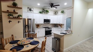 A modern kitchen with white cabinets, stainless steel appliances, and a dining area with a round table and chairs. - Wise Owl Retreat, a beautiful suite amongst towering oaks, access to River/view. (Dunnellon)